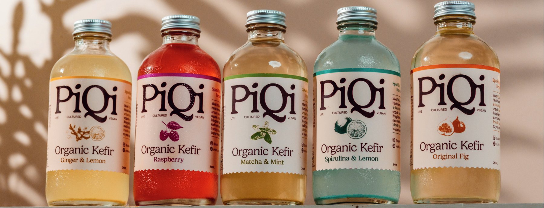 Five PiQi organic kefir bottles in a row: Ginger & Lemon, Raspberry, Matcha & Mint, Blue Spirulina & Lemon and Original Fig